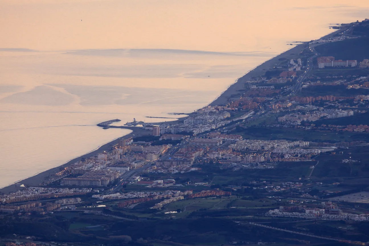San Luis de Sabinillas al atardecer, visto desde lo alto: el pueblo, la playa y el puerto de la Duquesa al fondo.